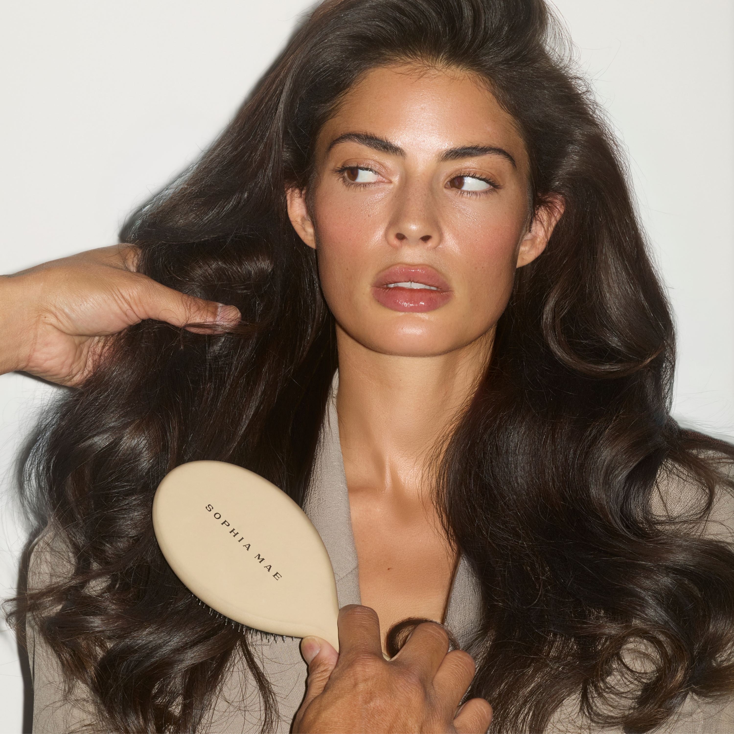 Model with thick brunette hair holding the beige SOPHIA MAE Hairbrush.