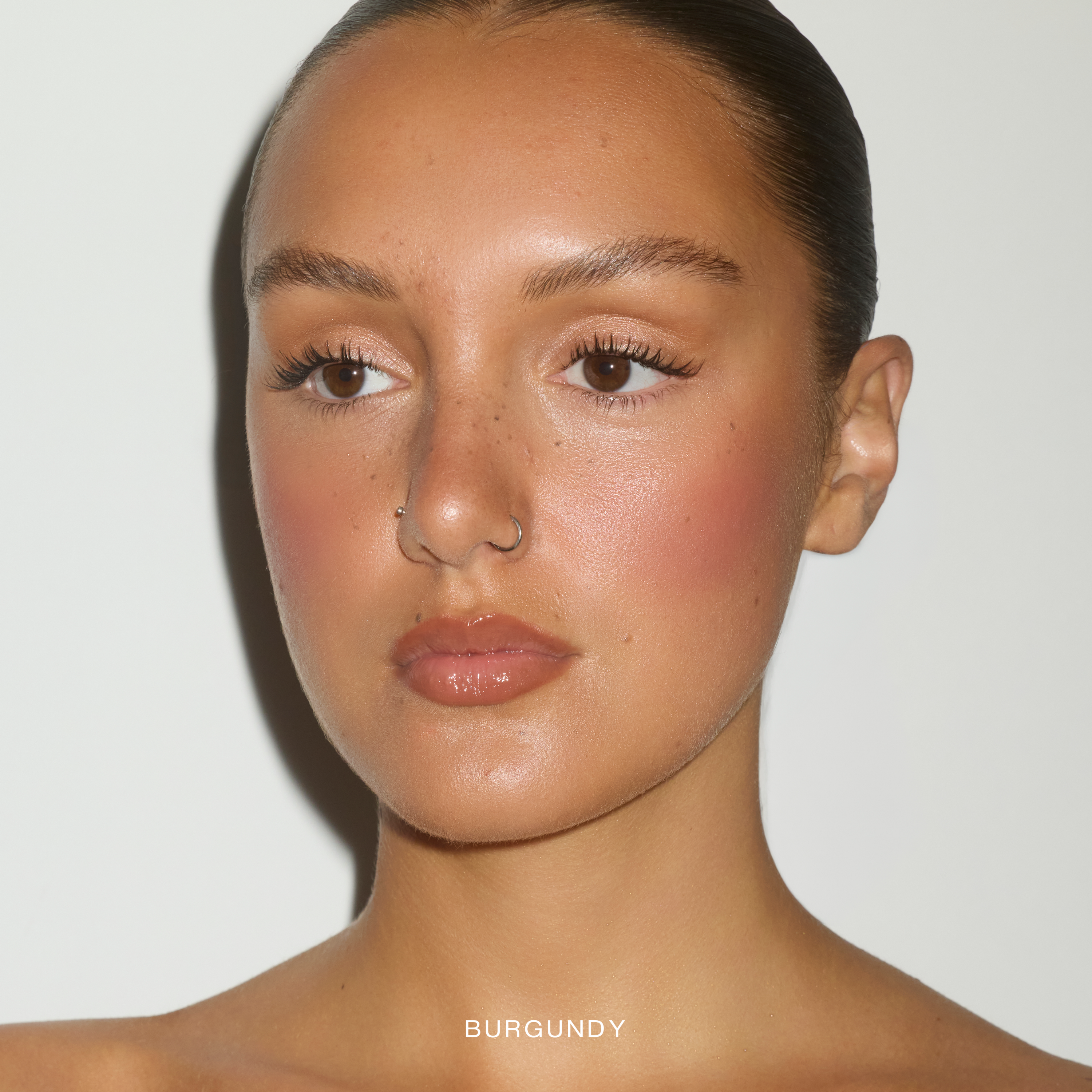 Model wearing SOPHIA MAE Cream Blush in the shade Burgundy Glow for a warm flushed look.