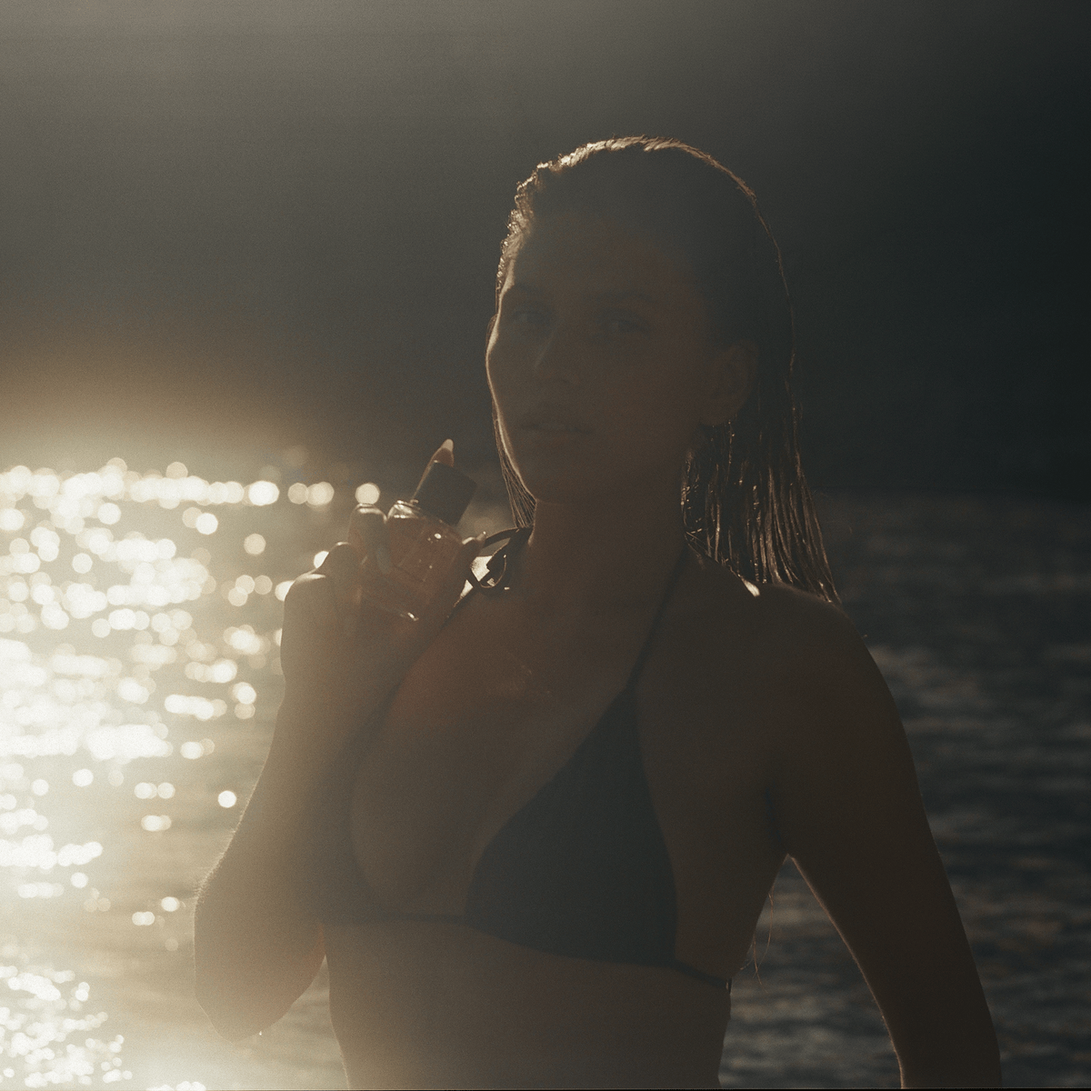 Written in Sand eau de parfum held against the neck beside the sea, captured in warm golden sunlight.
