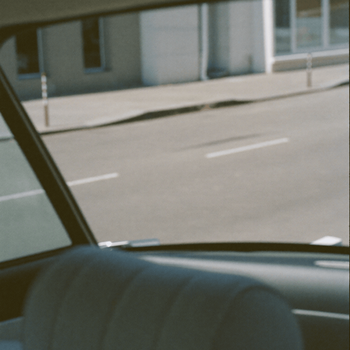 View of a city street through a car window, capturing the movement and understated energy of modern urban life.