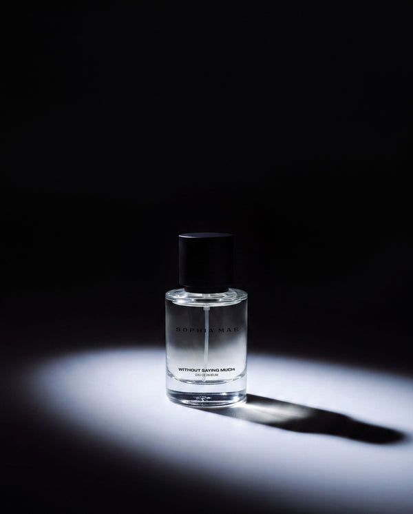 SOPHIA MAE Without Saying Much eau de parfum in a clear glass bottle, dramatically illuminated against a dark background.