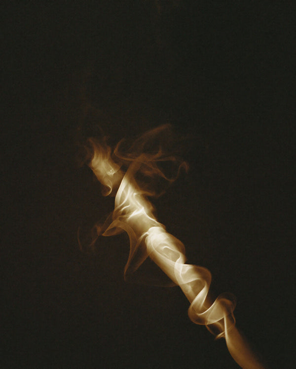 A sculptural trail of golden smoke twisting through the darkness, reflecting the warm and mysterious character of Without Saying Much eau de parfum.