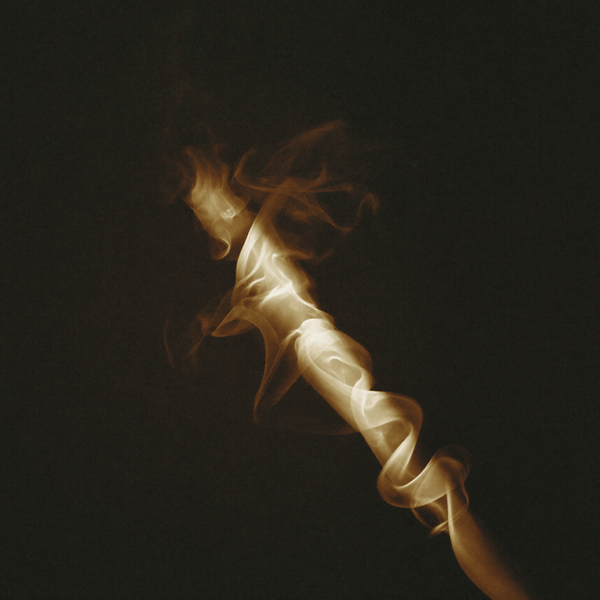 A sculptural trail of golden smoke twisting through the darkness, reflecting the warm and mysterious character of Without Saying Much eau de parfum.