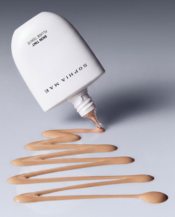 SOPHIA MAE Skin Tint dispensing onto a neutral surface, highlighting its fluid texture and lightweight, blendable formula.