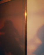 Warm blurred silhouette behind glass in soft amber light, evoking the intimate atmosphere of SOPHIA MAE Whispers of Elegance eau de parfum.