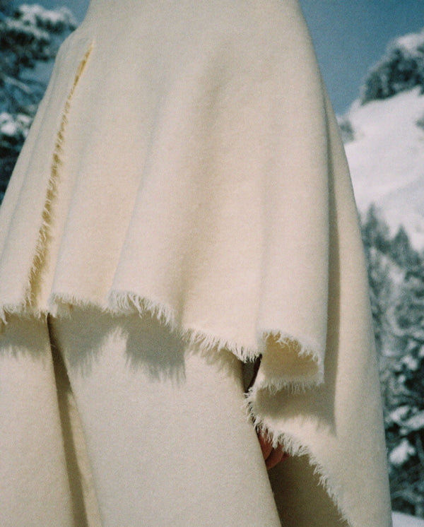 Soft fringed fabric beside a window overlooking snowy trees, capturing the winter atmosphere of Arctic Spice eau de parfum.