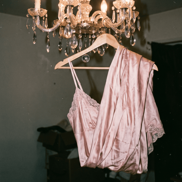 Pink satin lingerie hanging beneath a crystal chandelier, capturing the soft and intimate mood of Whispers of Elegance eau de parfum.