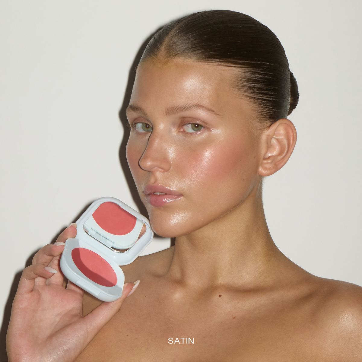 Model wearing SOPHIA MAE Cream Blush in the shade Satin Rose and holding the open compact.