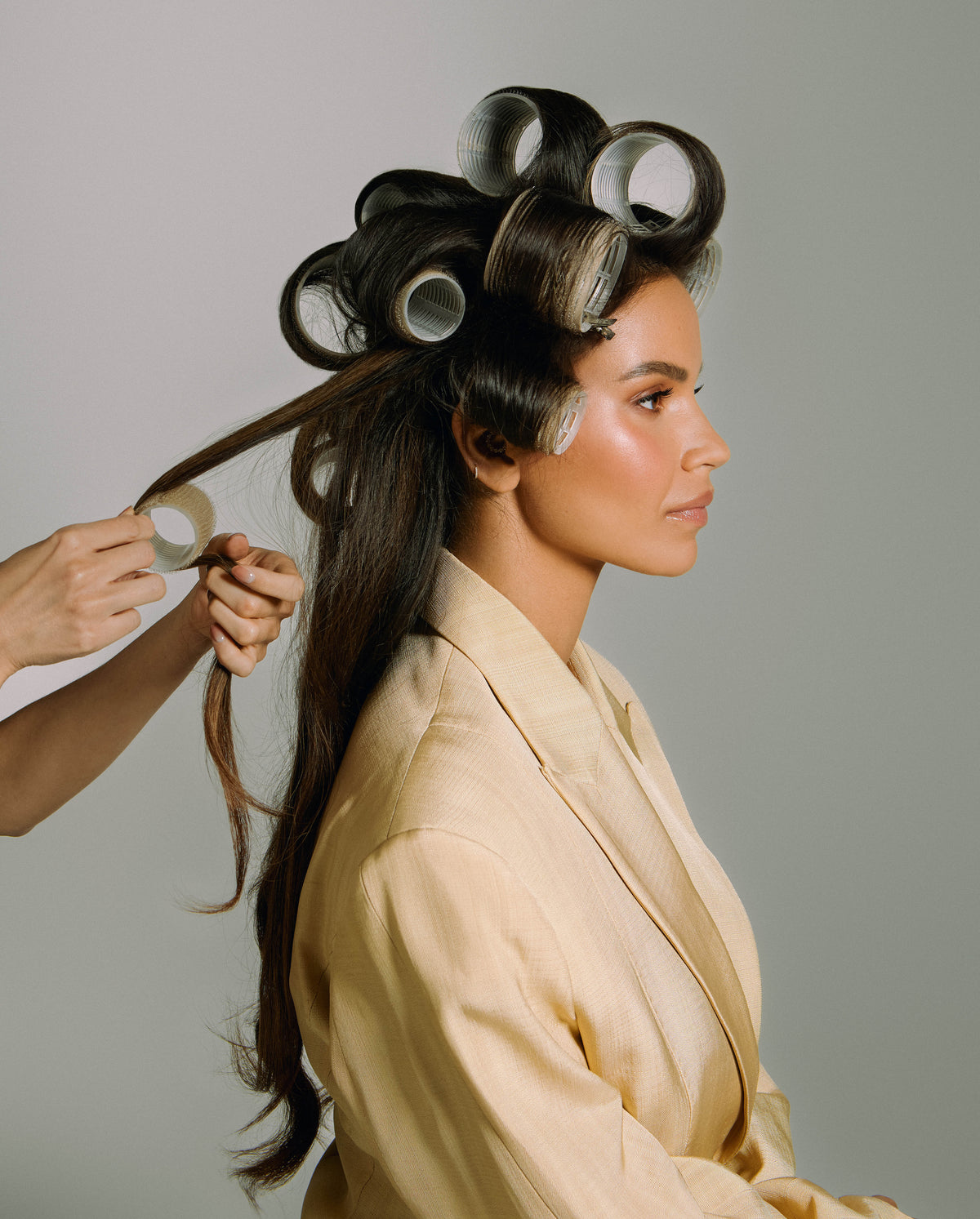 Monica Geuze being styled with SOPHIA MAE Velcro Hair Rollers, showing the rollers in place as another section is wrapped for added volume and shape.