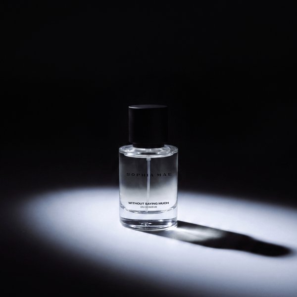 SOPHIA MAE Without Saying Much eau de parfum in a clear glass bottle, dramatically illuminated against a dark background.