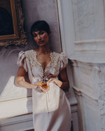Model in a satin lace dress holding SOPHIA MAE Still in Bloom Eau de Parfum in an elegant interior.