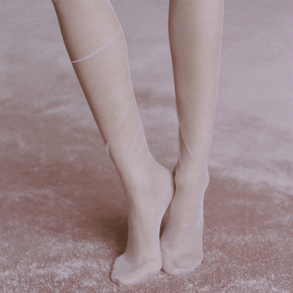 Close-up of legs in sheer ivory tights on a soft pink carpet, reflecting the delicate aesthetic of Whispers of Elegance eau de parfum.