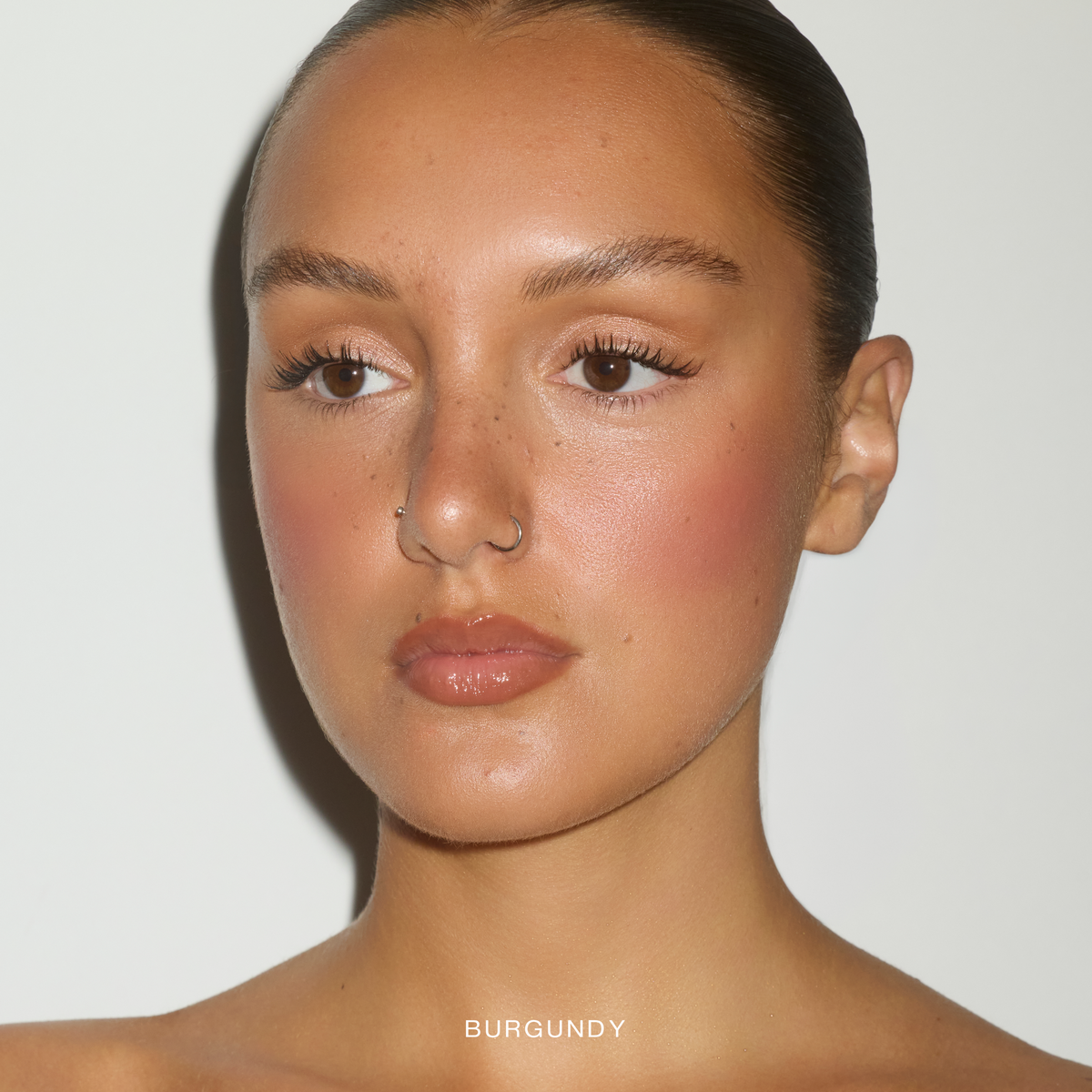 Model wearing SOPHIA MAE Cream Blush in the shade Burgundy Glow for a warm flushed look.