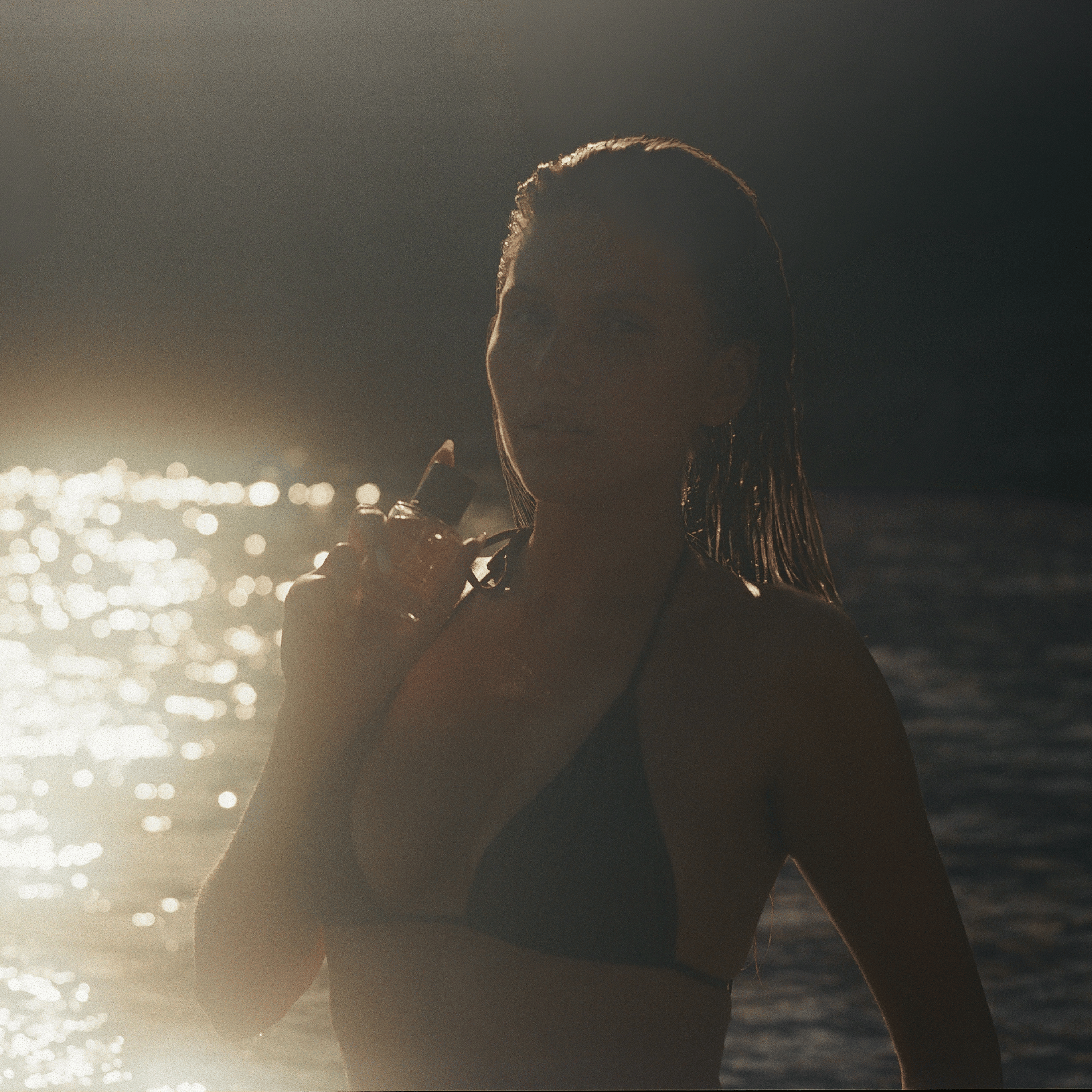 Written in Sand eau de parfum held against the neck beside the sea, captured in warm golden sunlight.