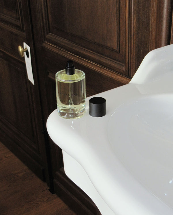 Golden Mirage perfume by SOPHIA MAE styled beside a bathtub in a warm, elegant bathroom setting.