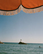 Ocean view beneath a striped parasol, capturing the sun-soaked mood of Golden Mirage perfume by SOPHIA MAE.