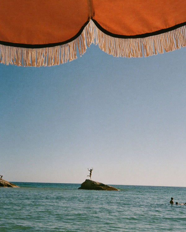 Ocean view beneath a striped parasol, capturing the sun-soaked mood of Golden Mirage perfume by SOPHIA MAE.