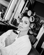 Monica Geuze wearing hair rollers while holding a SOPHIA MAE Travel Mug in a beauty setting.