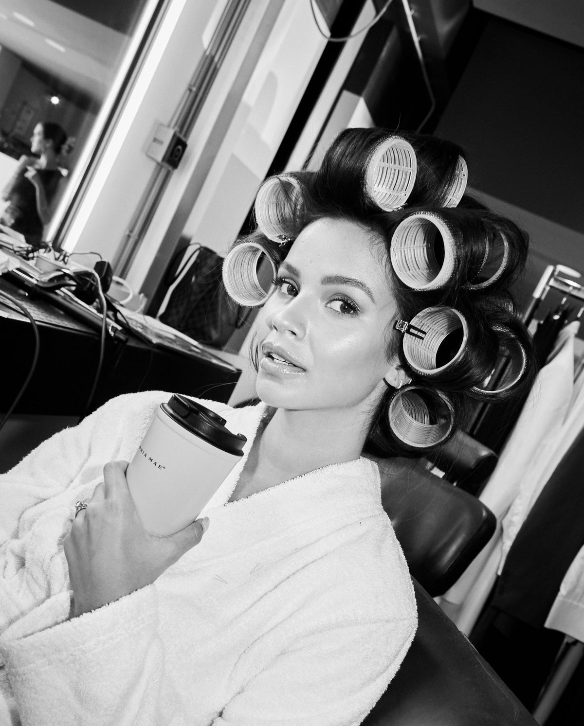 Monica Geuze wearing hair rollers while holding a SOPHIA MAE Travel Mug in a beauty setting.