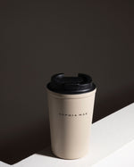 SOPHIA MAE Travel Mug in cream with black lid, styled on a minimal neutral surface.