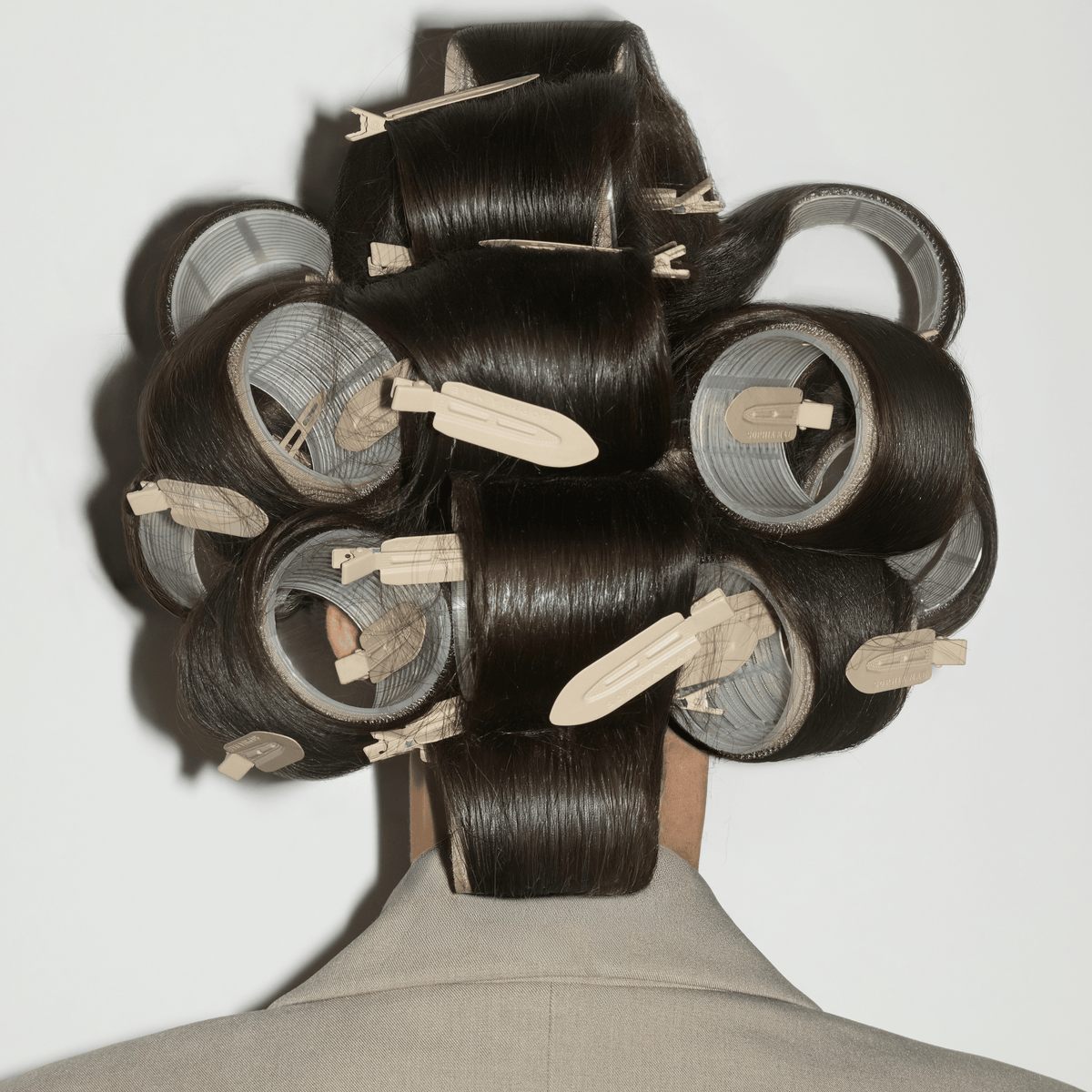 Back view of glossy dark hair wrapped around large rollers and secured with beige SOPHIA MAE Creaseless Hair Clips.