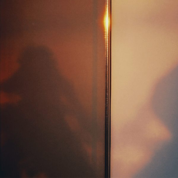 Warm blurred silhouette behind glass in soft amber light, evoking the intimate atmosphere of SOPHIA MAE Whispers of Elegance eau de parfum.