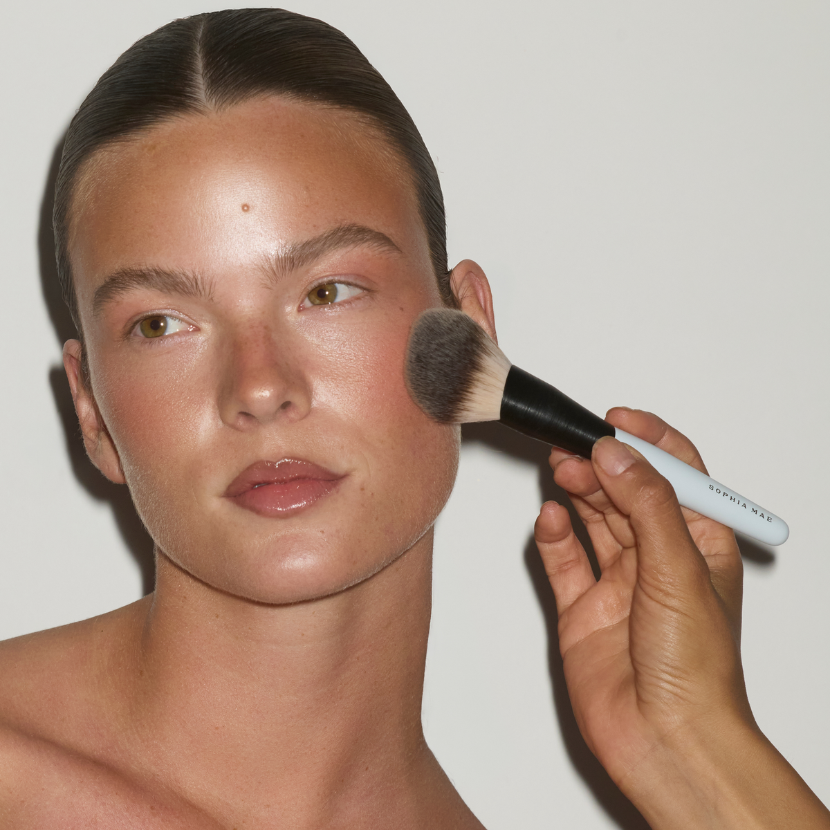 Bronzing powder being applied to a model’s cheek with the SOPHIA MAE Powder Brush.