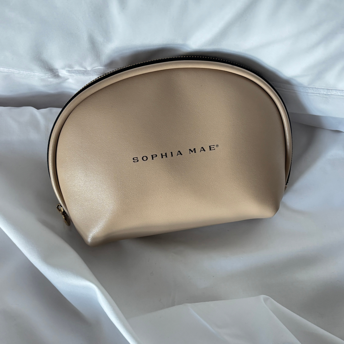 Beige SOPHIA MAE Beauty Bag with zipper displayed on white bed linen.