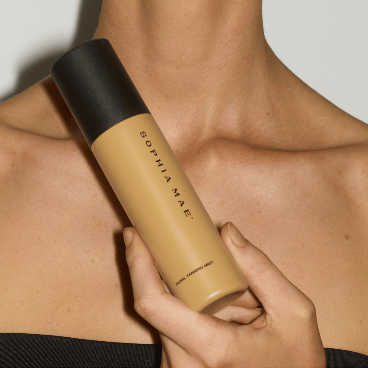 Close-up of the SOPHIA MAE Facial Tanning Mist held against a warm, sun-kissed décolletage.