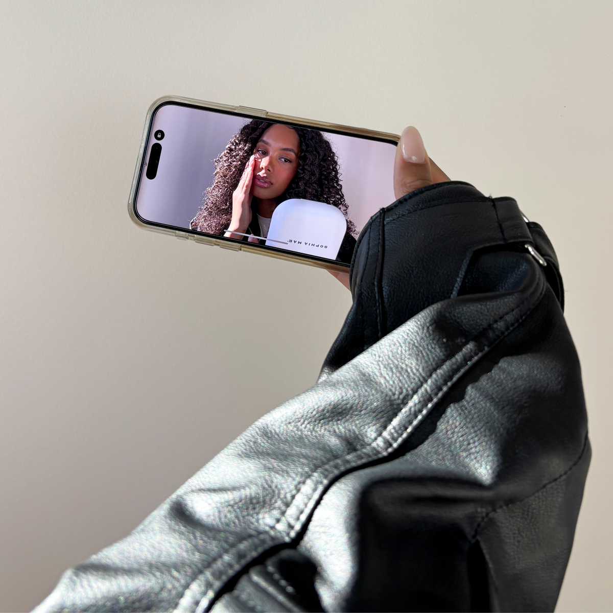 Person applying SOPHIA MAE Cream Blush with smartphone face camera.