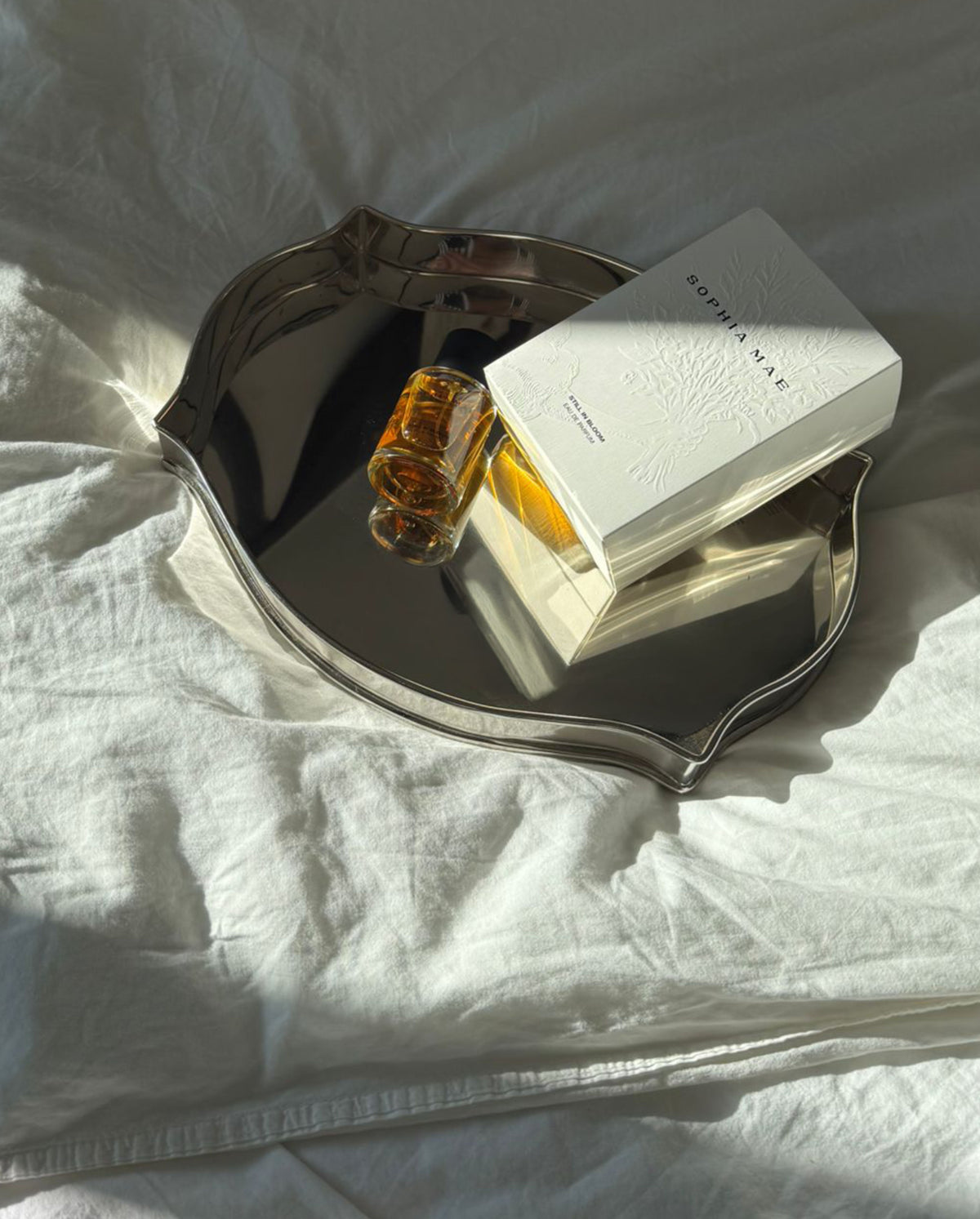 SOPHIA MAE Still in Bloom Eau de Parfum bottle and packaging displayed on a silver tray in soft sunlight.