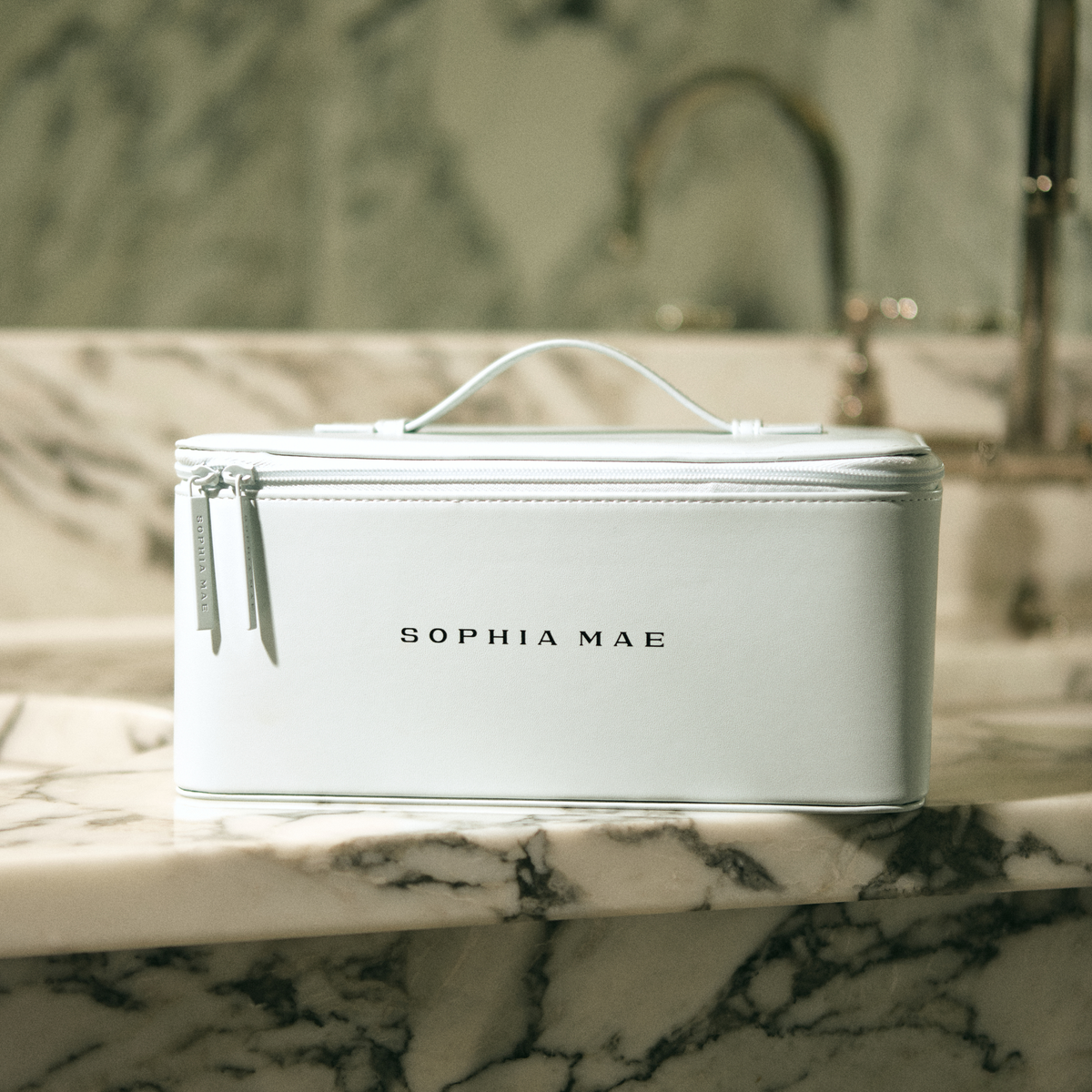 Closed white SOPHIA MAE Beauty Organizer with handle and double zip closure on a marble bathroom counter.