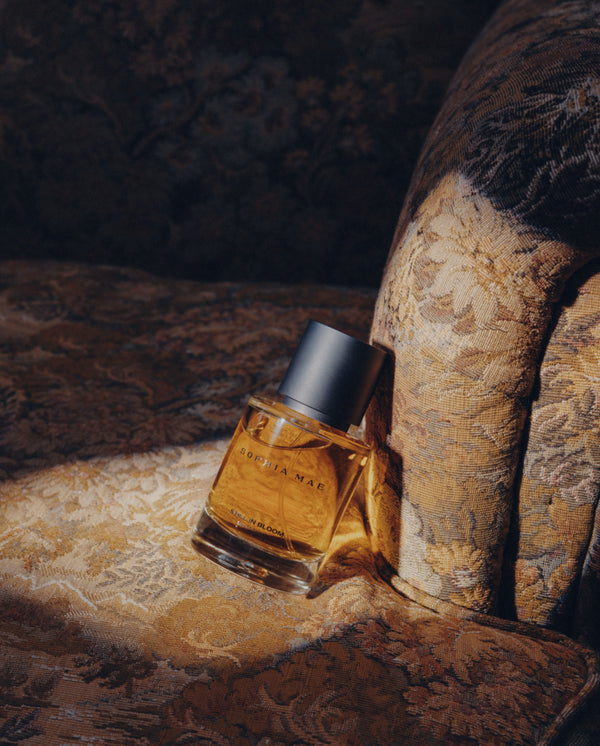 SOPHIA MAE Still in Bloom Eau de Parfum bottle resting on a vintage floral armchair.