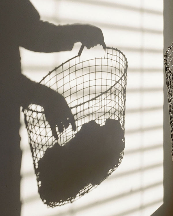 Shadow on a wall of a person holding a wire laundry basket in warm sunlight.