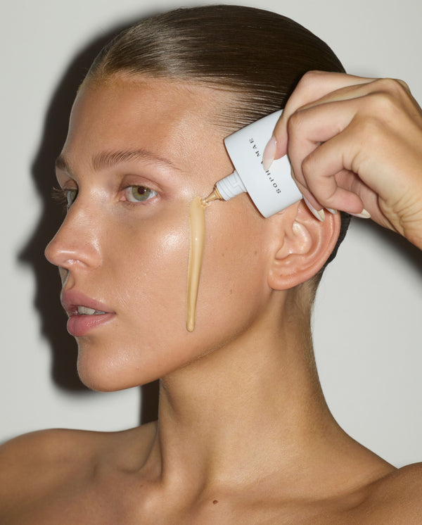 Close-up of a model applying SOPHIA MAE Skin Tint to her cheek, showing its lightweight texture and natural, dewy glow.