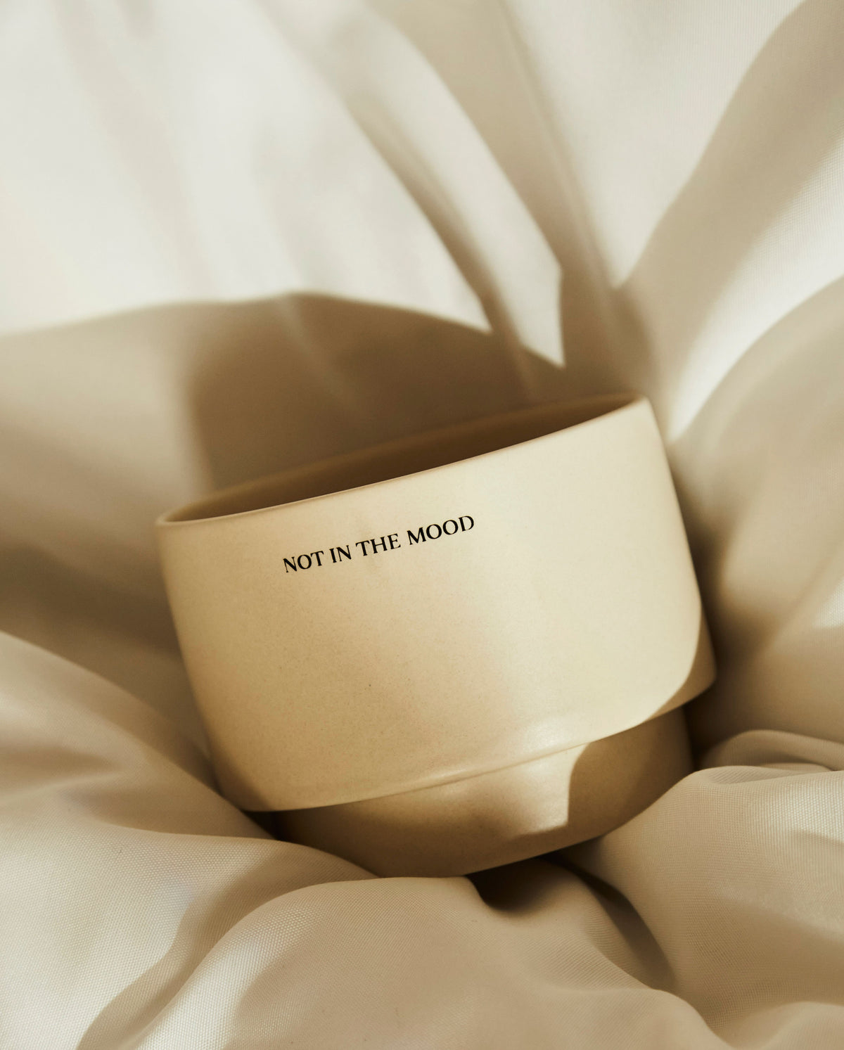 Close-up of the SOPHIA MAE moody mug surrounded by soft white bedding. With the text not in the mood. 