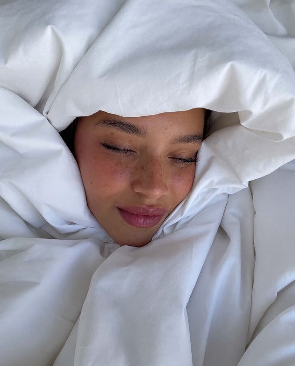 Close-up of a woman sleeping peacefully wrapped in soft, white bed sheets.
