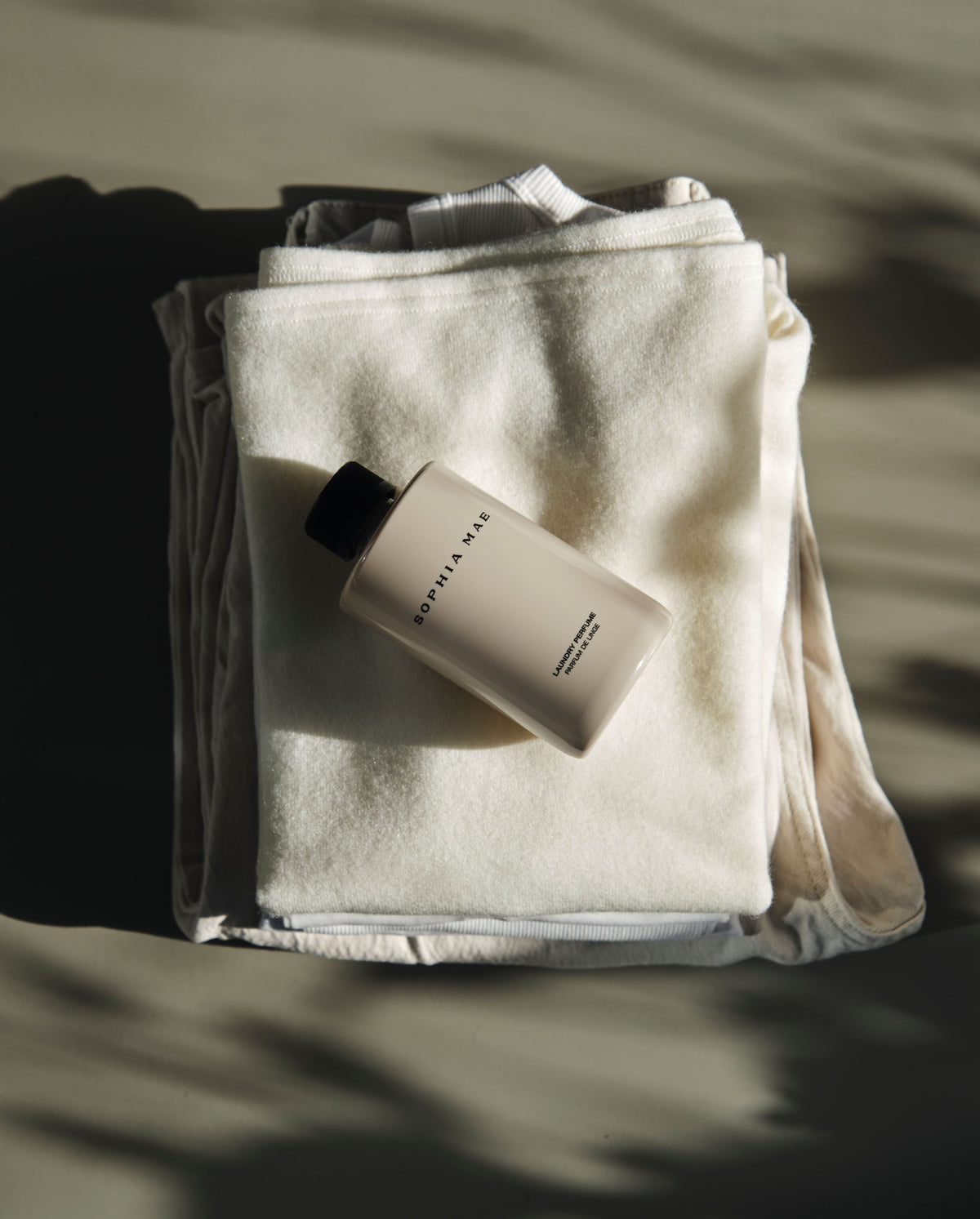 Dew of dawn laundry perfume by SOPHIA MAE laying on fresh beige clothes. 