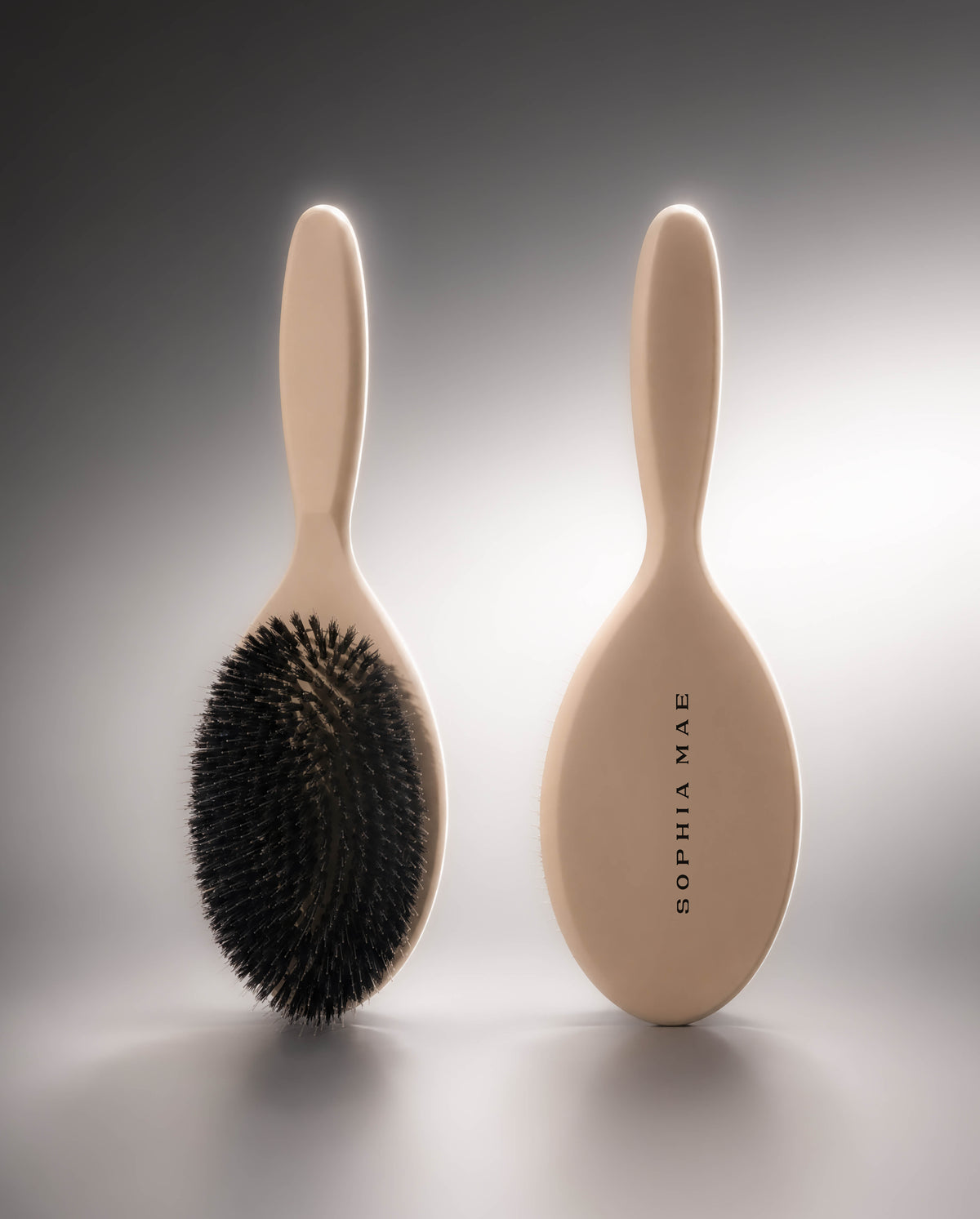 SOPHIA MAE Hairbrush shown from the front and back, featuring dense black boar bristles and a smooth beige handle with signature branding.
