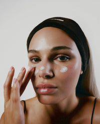 Close-up of model applying skincare while wearing a black SOPHIA MAE headband.