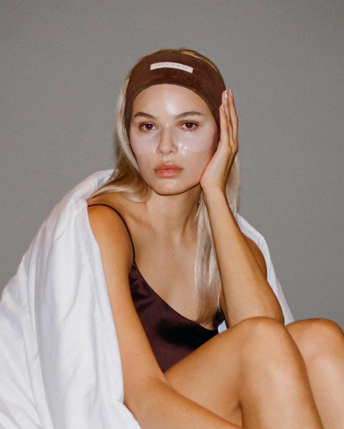 Model wearing a brown SOPHIA MAE headband during her skincare routine.