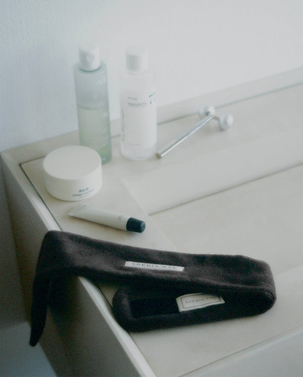 Brown SOPHIA MAE headband styled with skincare products on a bathroom counter.