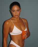 Model in a white bikini holding a tube of SOPHIA MAE Body Tanning Cream.