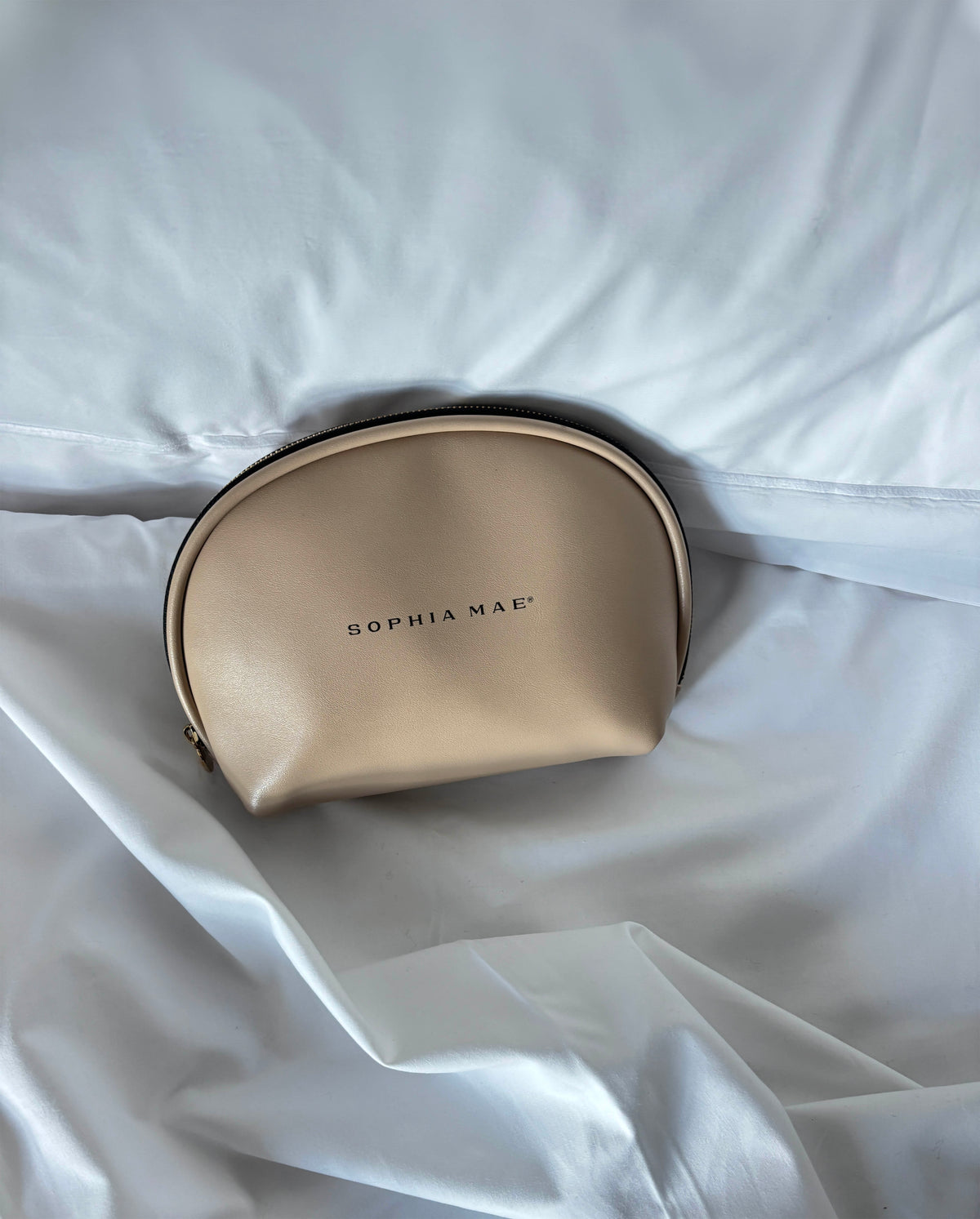 SOPHIA MAE Beauty Bag in beige, styled on soft white bedding.