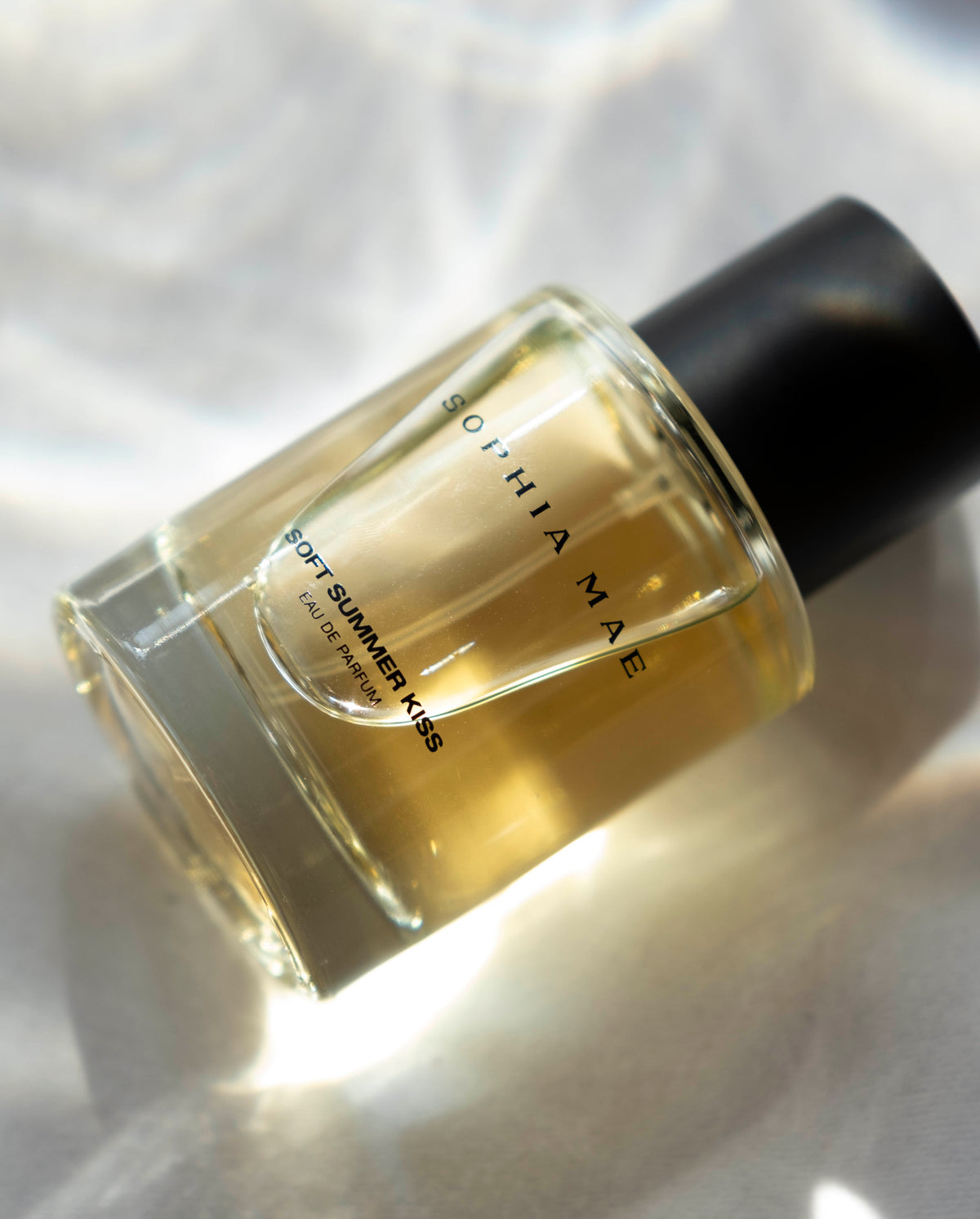 SOPHIA MAE Soft Summer Kiss EDP bottle glowing in soft sunlight on white fabric.