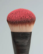 Close-up of the SOPHIA MAE Liquid Blending Brush with dense bristles coated in blush, showing the brush shape and product pickup.
