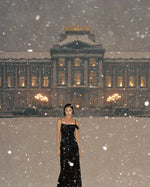 Model in a black dress standing in falling snow for SOPHIA MAE Arctic Spice perfume.