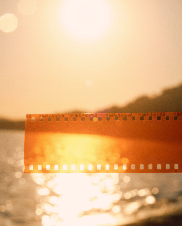 Golden film strip glowing in a seaside sunset, inspired by SOPHIA MAE Written in Sand Eau de Parfum and Body & Hair elixir. 