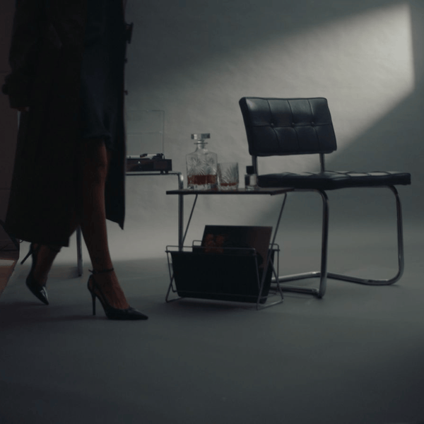 A minimal interior with a black leather chair, record player and perfume bottle, lit by a single beam of light.