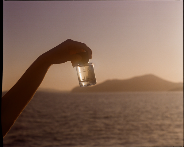 SOPHIA MAE Written in Sand Eau de Parfum bottle held against a golden sunset over the sea.